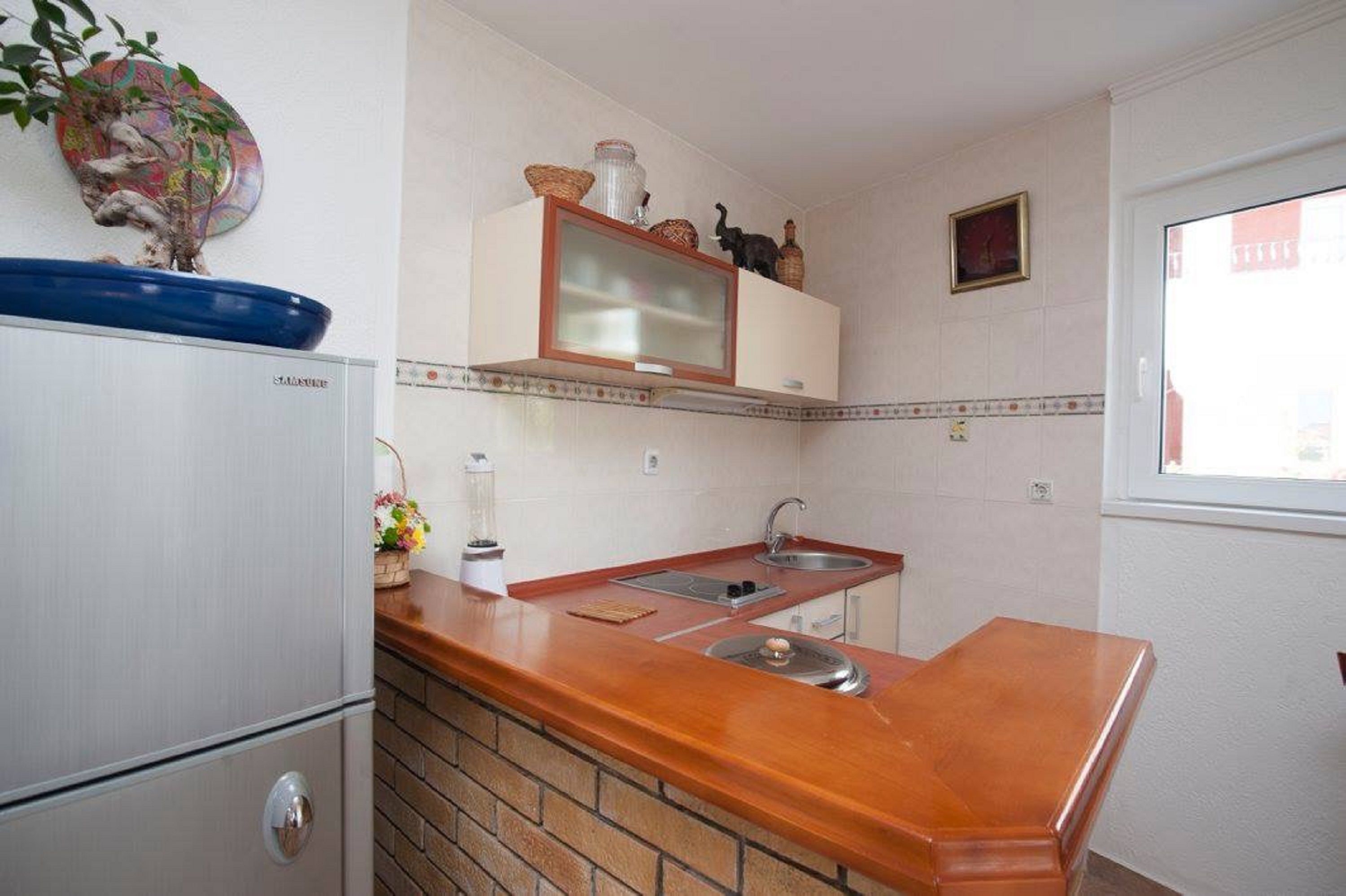 Een praktische keuken met een koelkast, een dubbele spoelbak en een houten aanrecht.