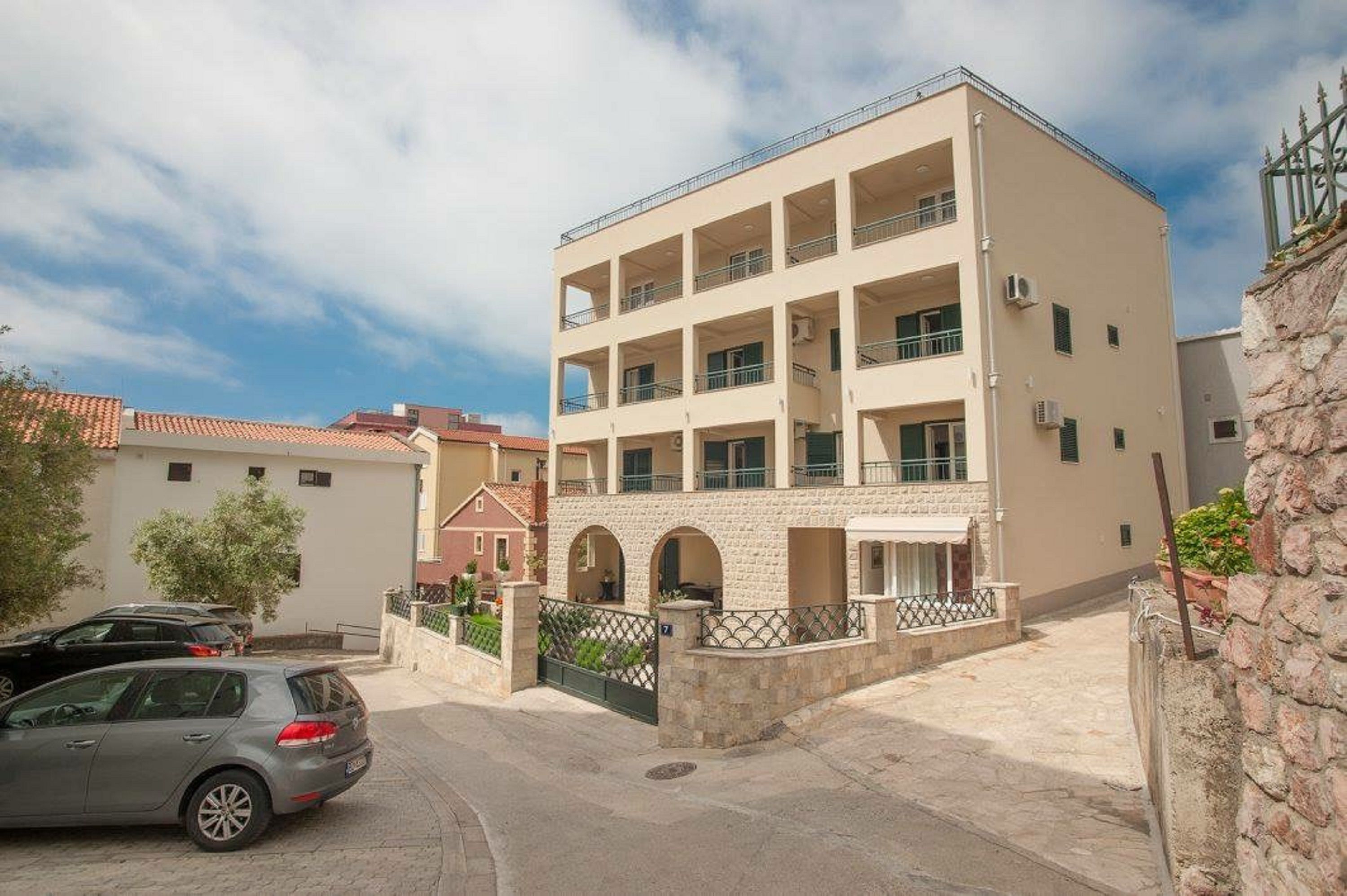 A multi-story building with balconies, a gated entrance, and a parking area.