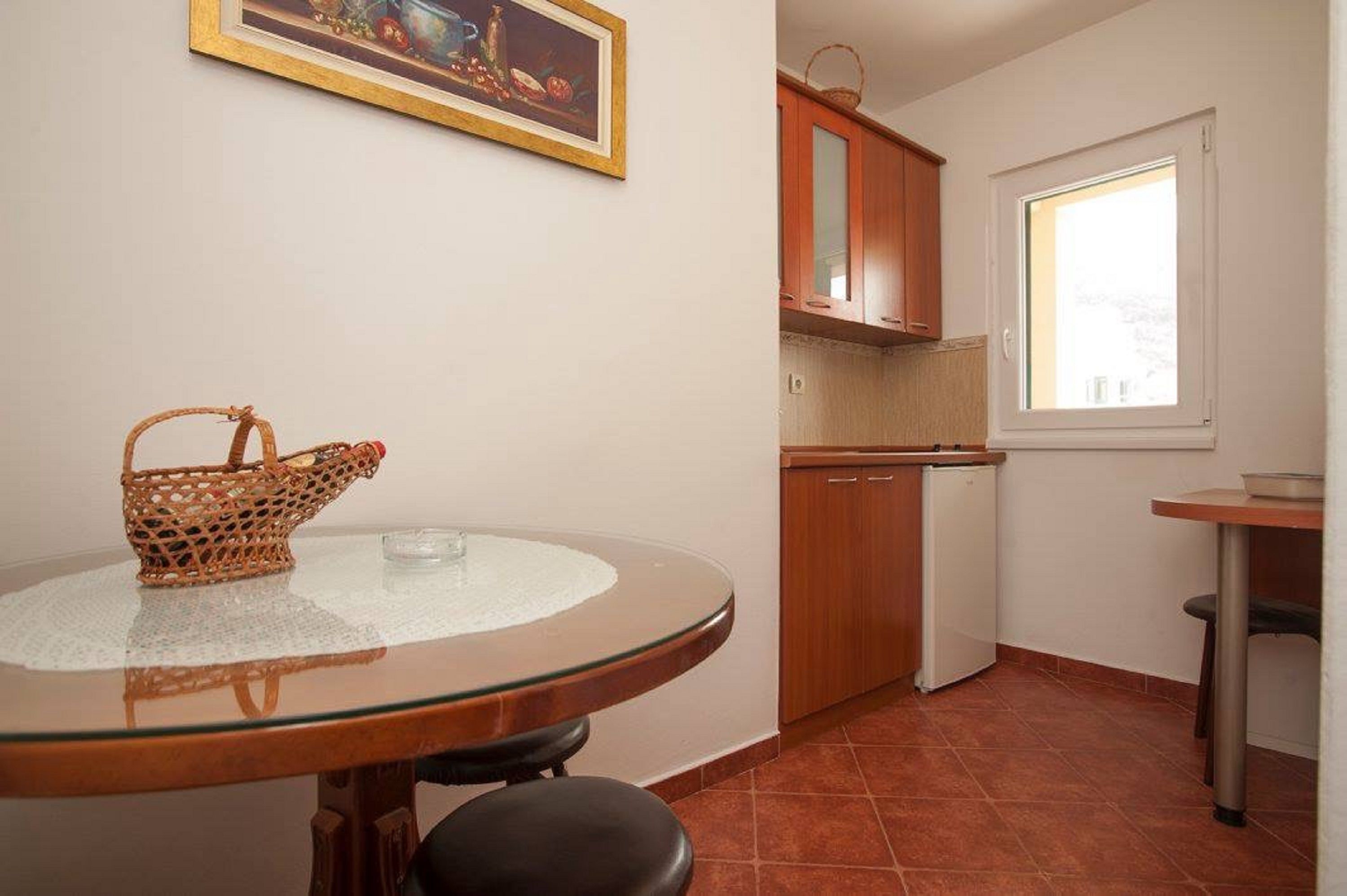 Una cocina compacta con una mesa redonda de vidrio, una cesta de mimbre y armarios de madera.