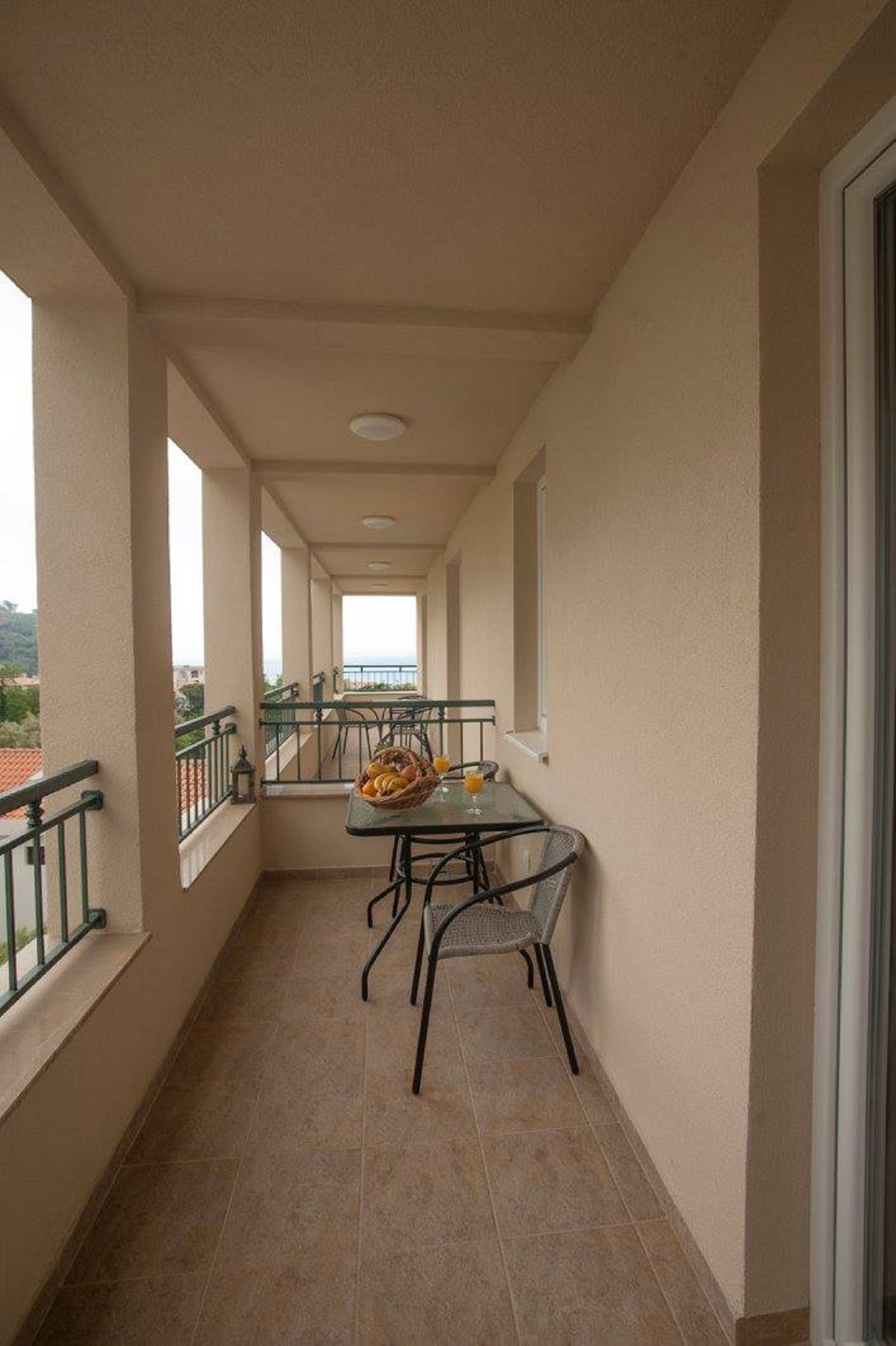 A narrow balcony with a table and chairs, a basket of fruit, and a view of the sea.