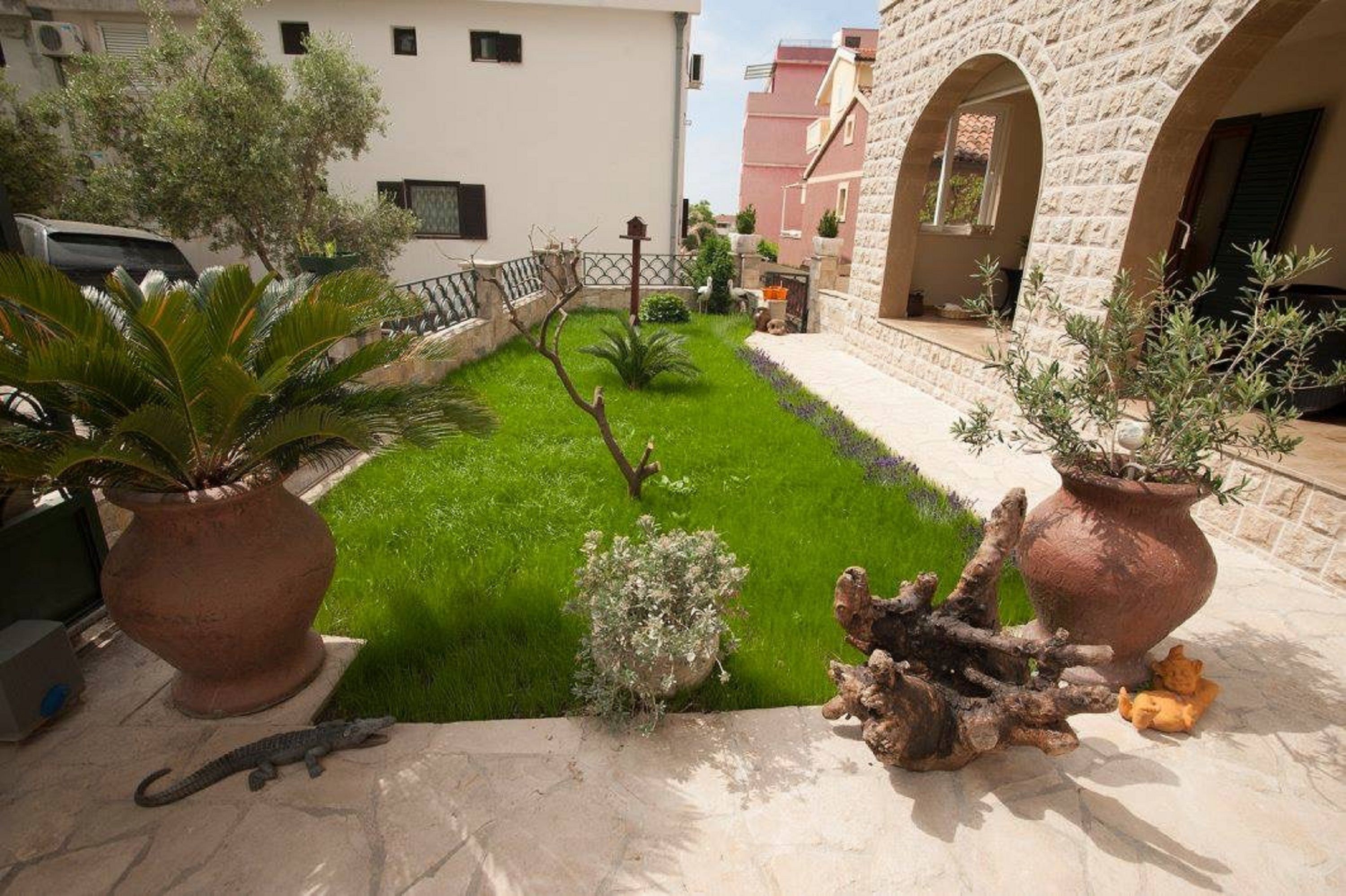 Un patio con césped cuidado, plantas en macetas y un tronco de árbol decorativo.