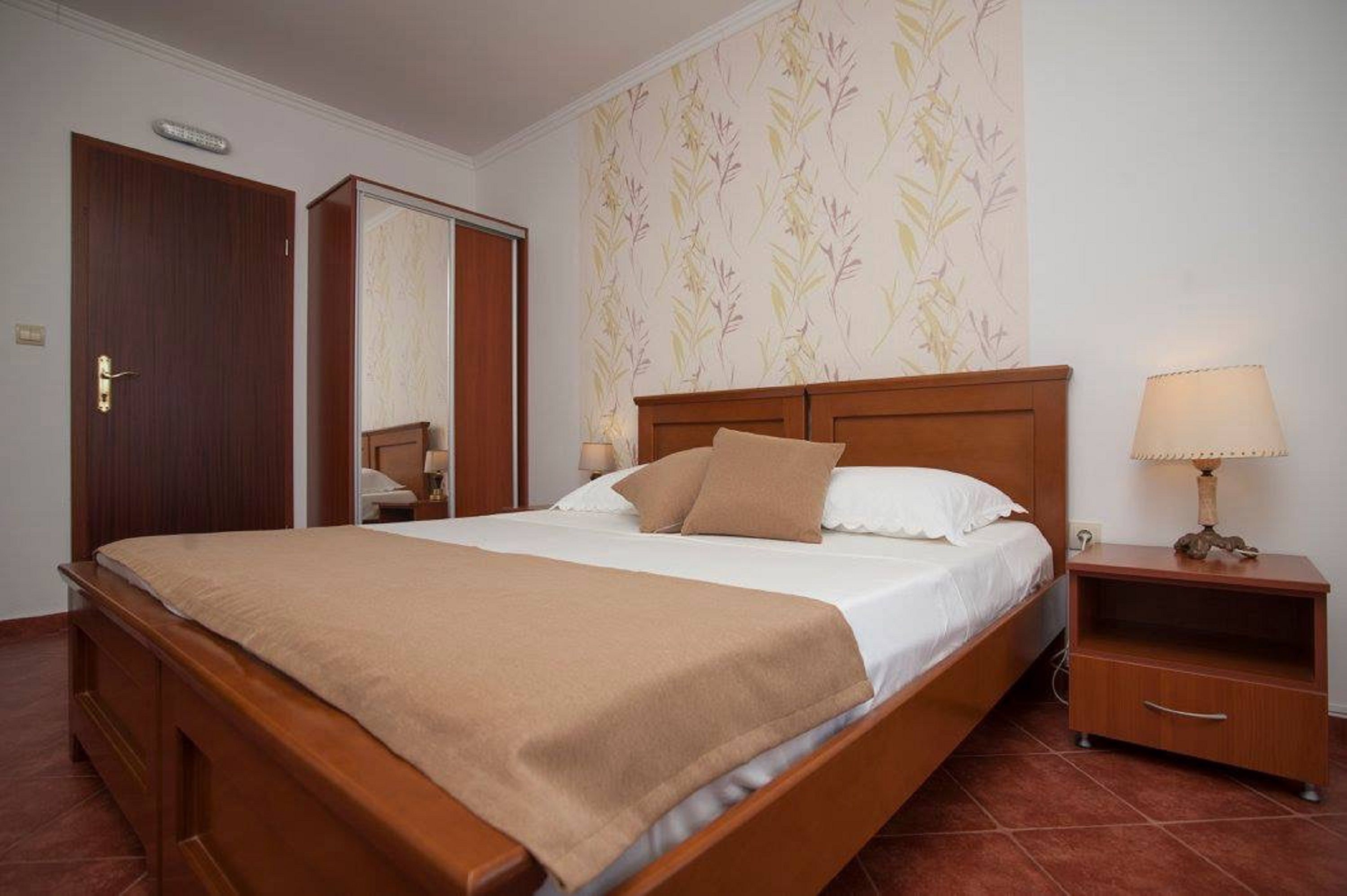 A neatly made bed with a wooden headboard, a bedside table with a lamp, and a wardrobe with a mirror.