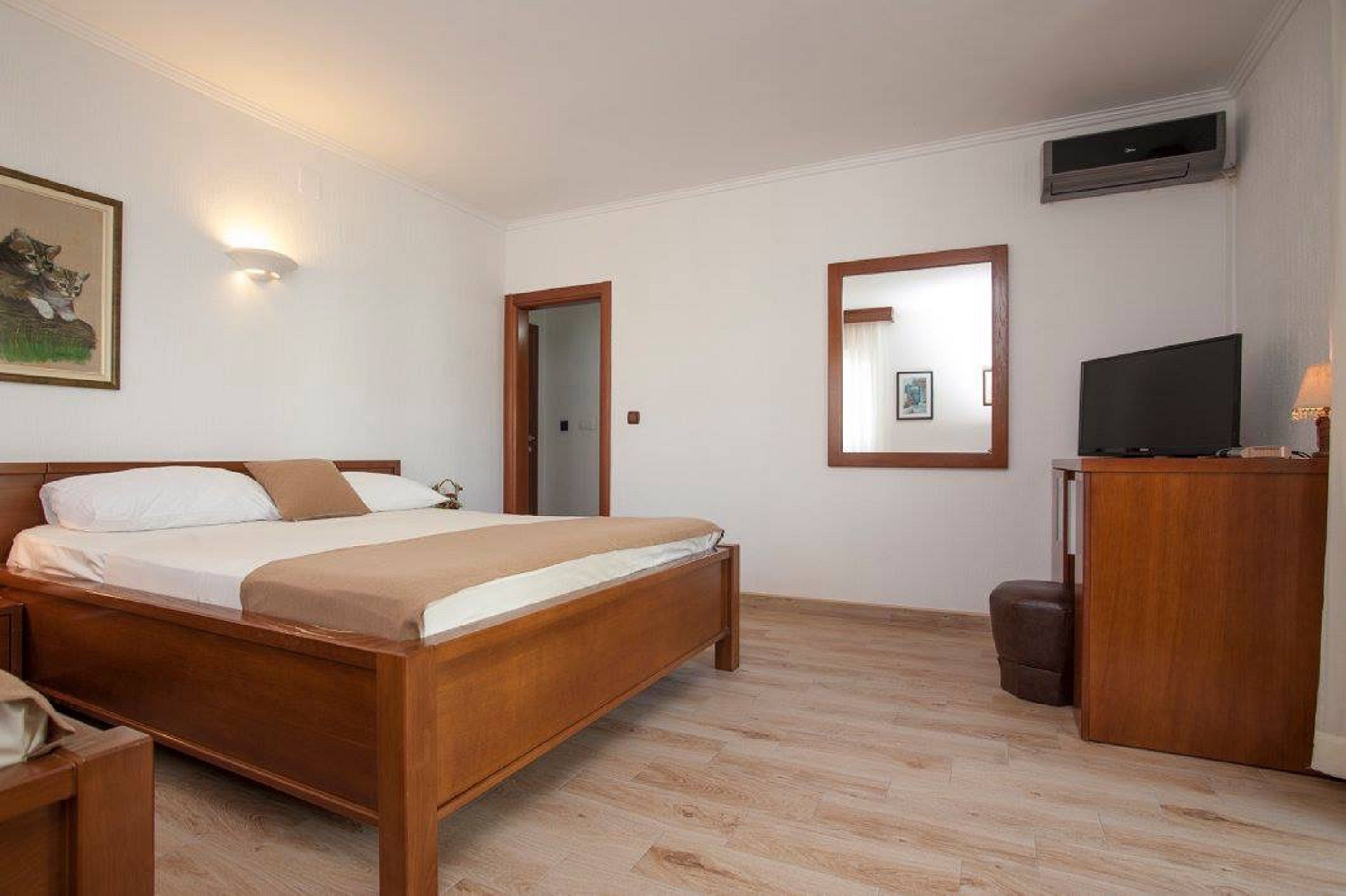 A hotel room with a wooden bed, a desk with a television, and a mirror on the wall.