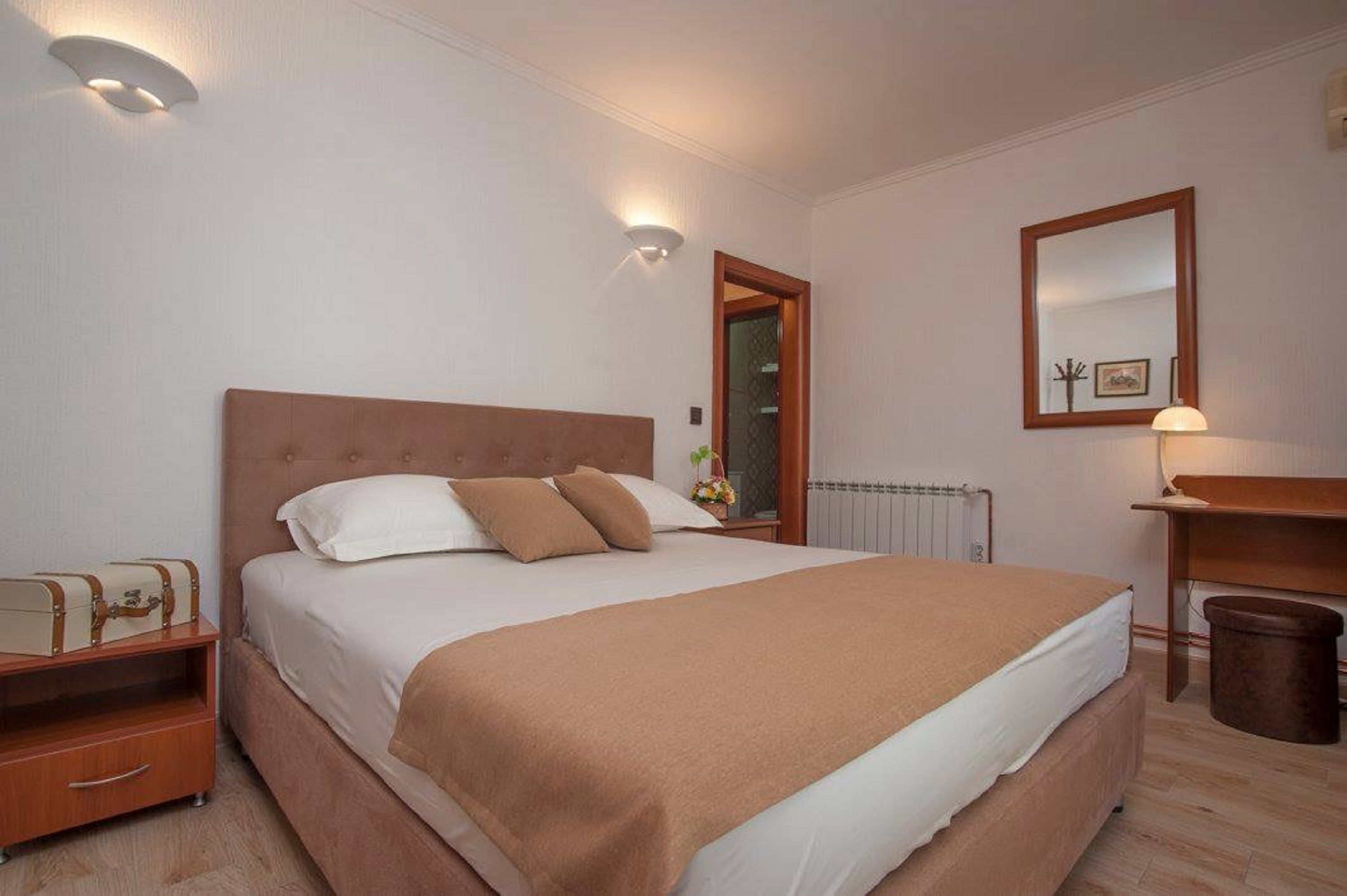 Ein ordentlich eingerichtetes Schlafzimmer mit einem großen Bett, Nachttischen, einem Spiegel und einem Heizkörper.