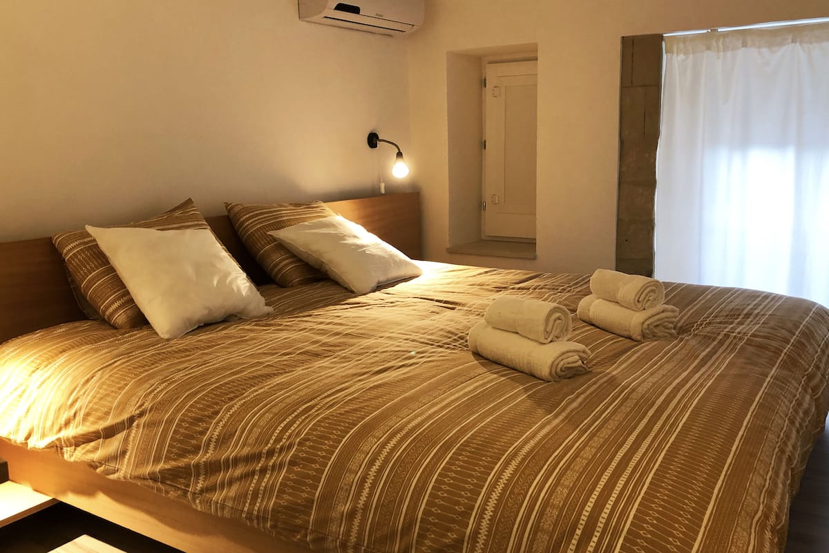 A neatly made bed with striped bedding and pillows, a bedside lamp, and rolled towels on the bed.