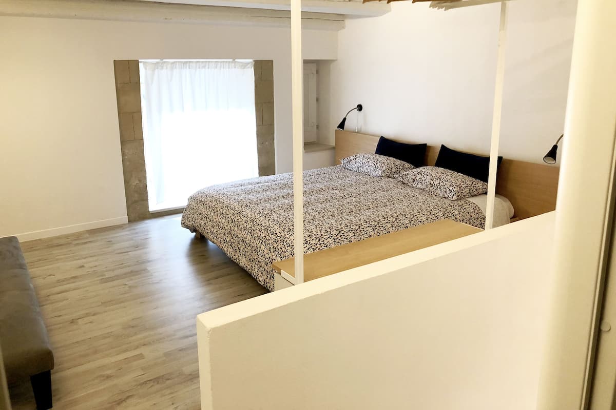 A bedroom with a bed, a wooden bench, a hanging clothes rack, and a window with curtains.