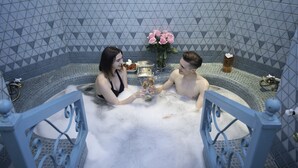 A couple in a jacuzzi with a decorative vase of flowers and a bottle of champagne. - Best Location 7BR Next to FR Quarter! By YouRent (New Orleans)