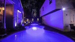A swimming pool with a hot tub in the center, surrounded by two-story houses with exterior lighting. - Best Location 7BR Next to FR Quarter! By YouRent (New Orleans)