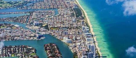 Vue aérienne d’une ville côtière avec une zone urbaine densément peuplée, une longue plage et un port de plaisance.
