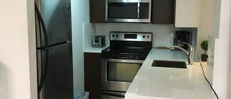 A modern kitchen with stainless steel appliances, a white countertop, and a bar stool.