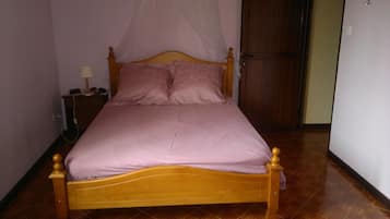 A single bed with a wooden frame and a canopy, a bedside table with a lamp, and a door in the background.
