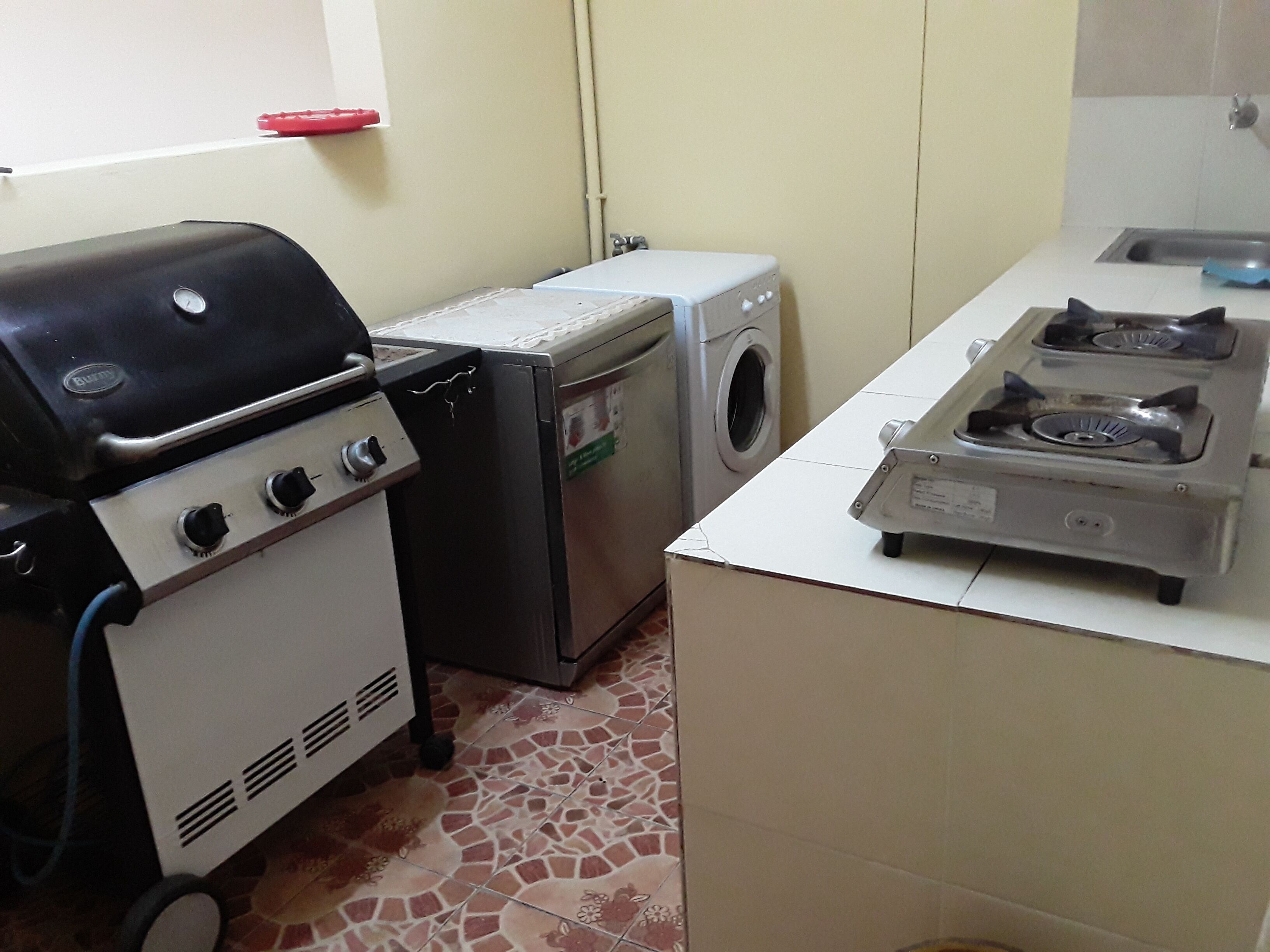 A compact kitchen with a gas stove, a washing machine, and a small refrigerator.