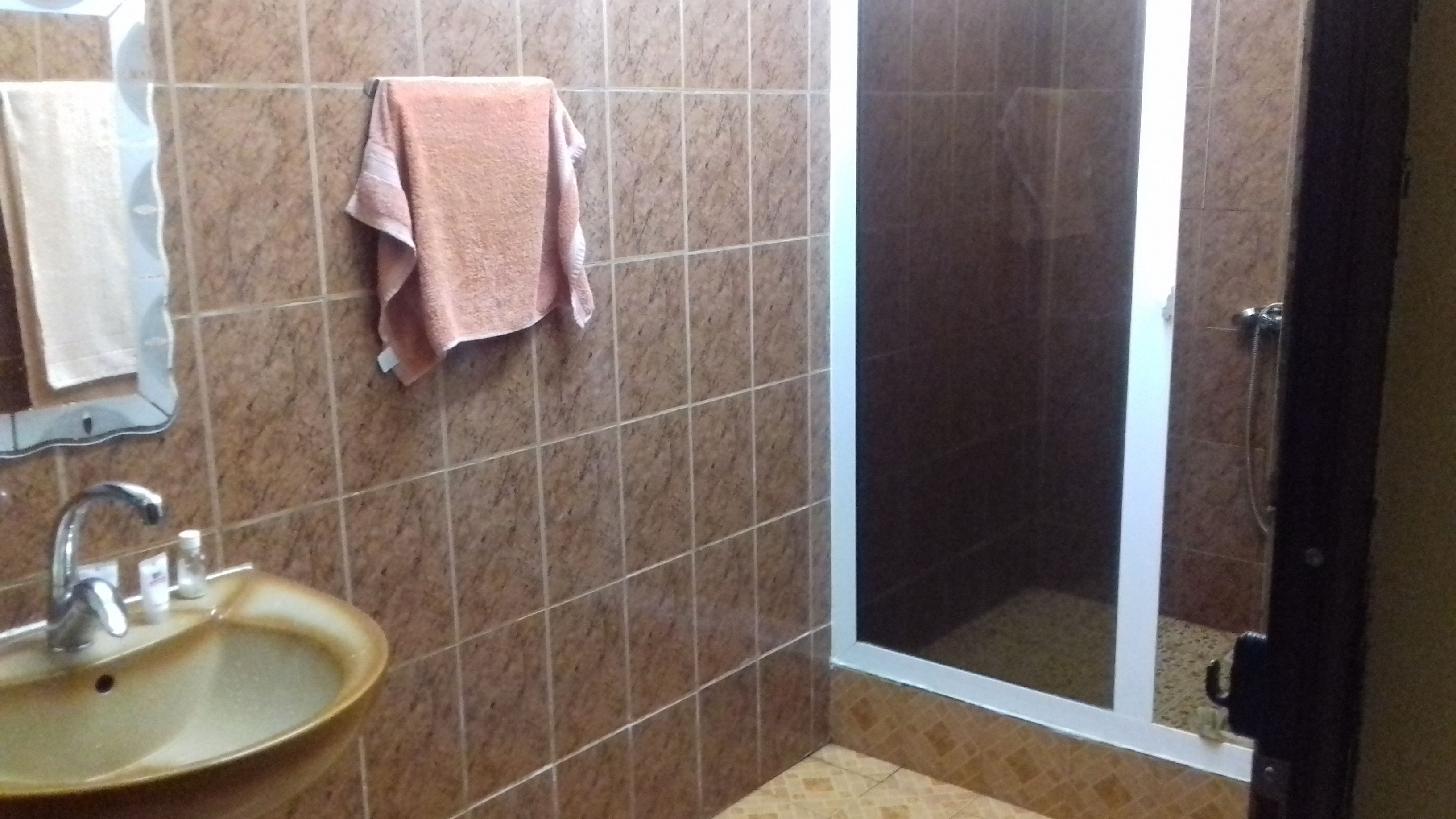 A bathroom with a sink, a mirror, a shower, and a towel hanging on the wall.