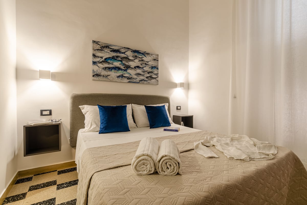 A hotel room with a bed, two bedside tables, a wall-mounted artwork, and a checkered floor.
