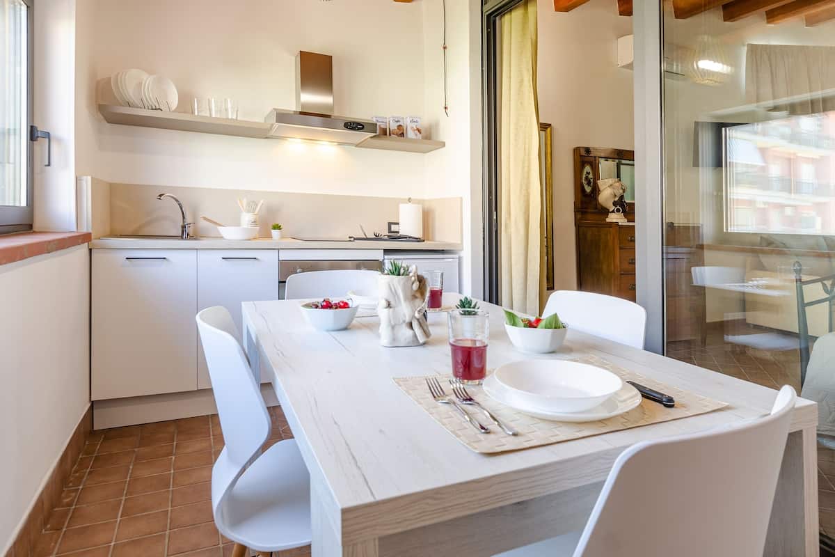 A modern kitchen with white cabinets, a dining table set with plates, cutlery, and a glass of red drink.