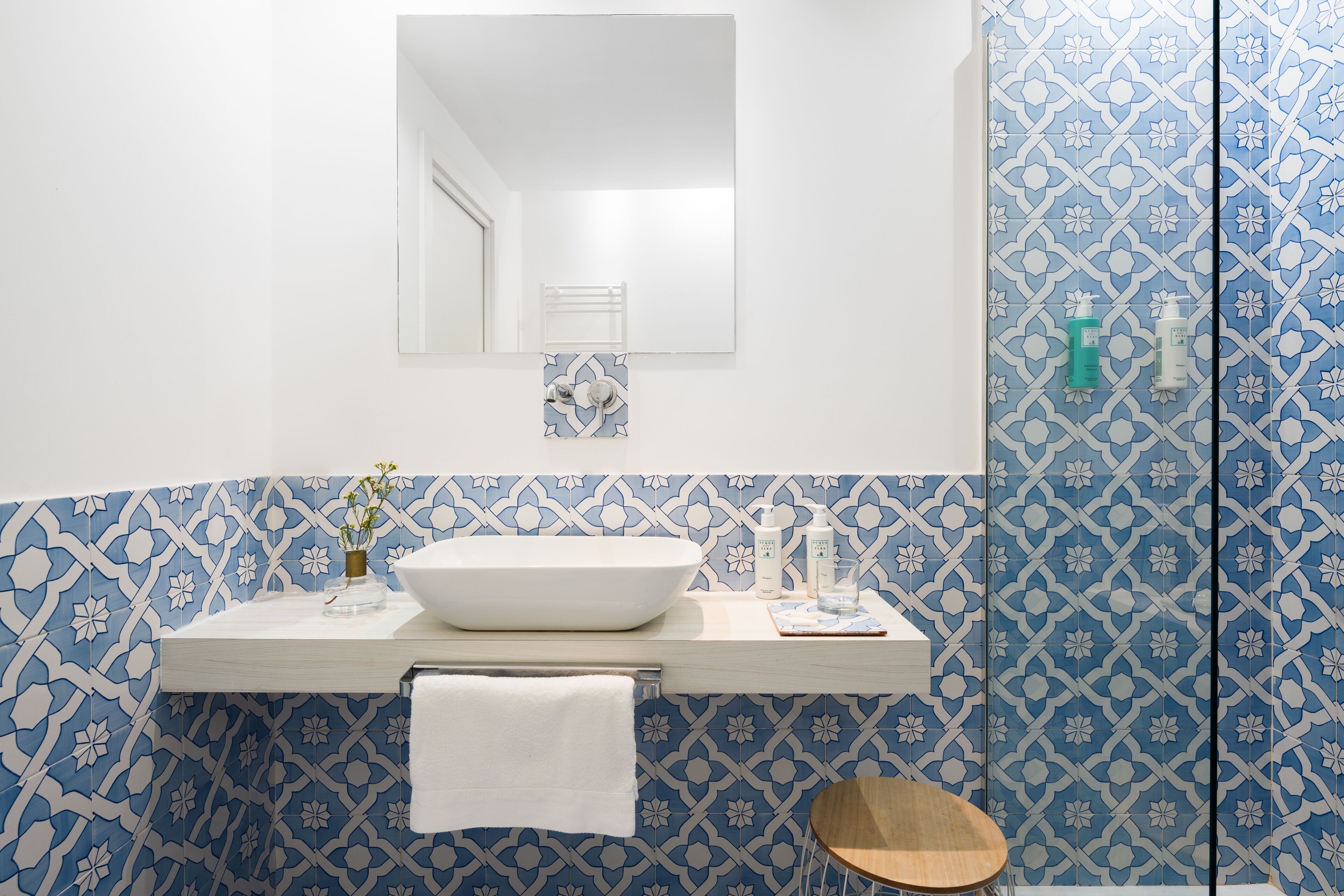 Une salle de bain avec un lavabo blanc, un miroir et un mur à motifs bleus.