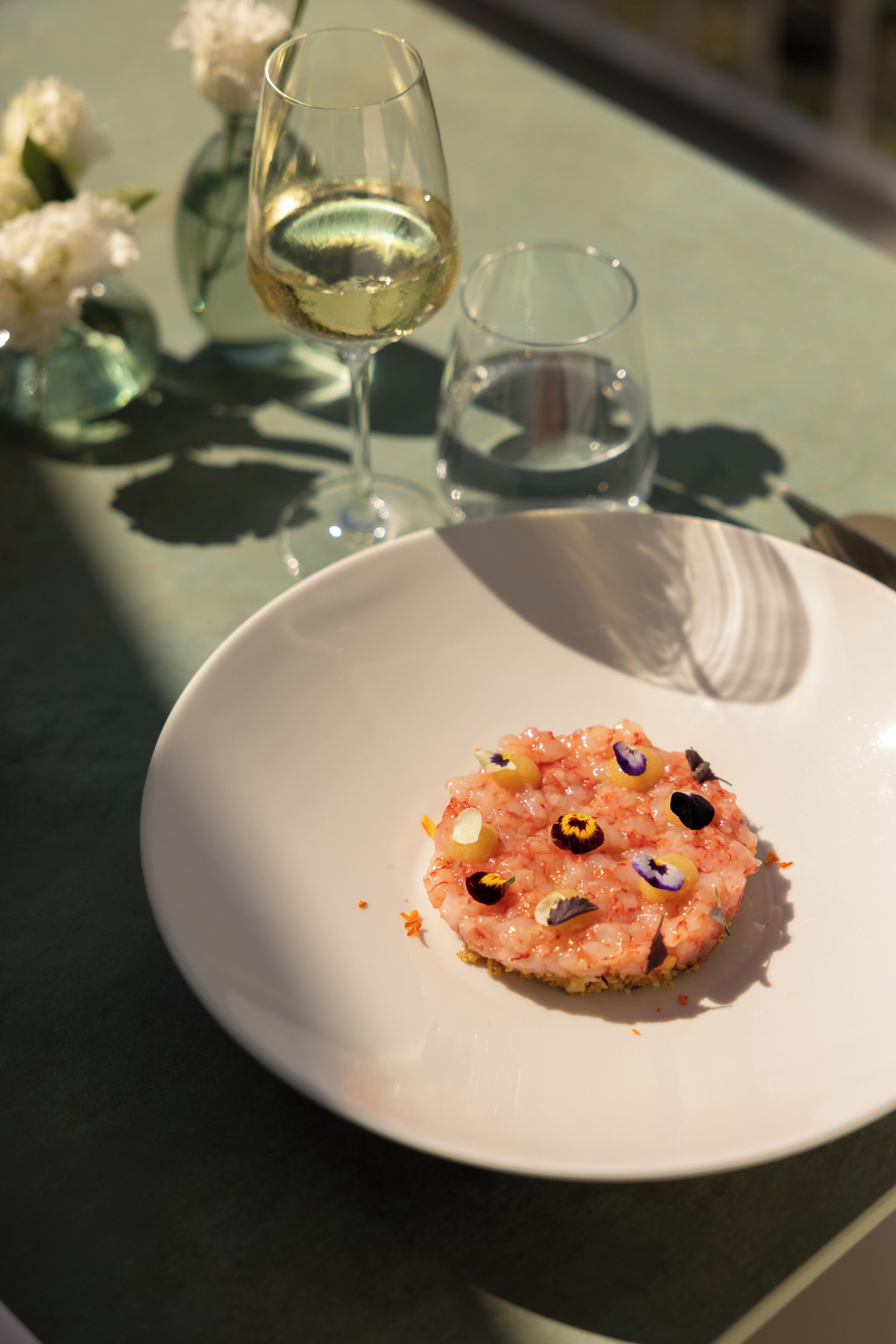A white plate with a seafood dish, a glass of white wine, and a small glass of water on a table.