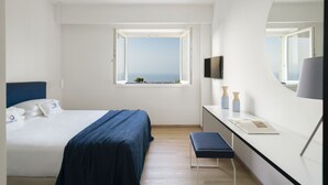 Un hotel moderno con cama, escritorio, banca, espejo grande y ventana con vista al mar.