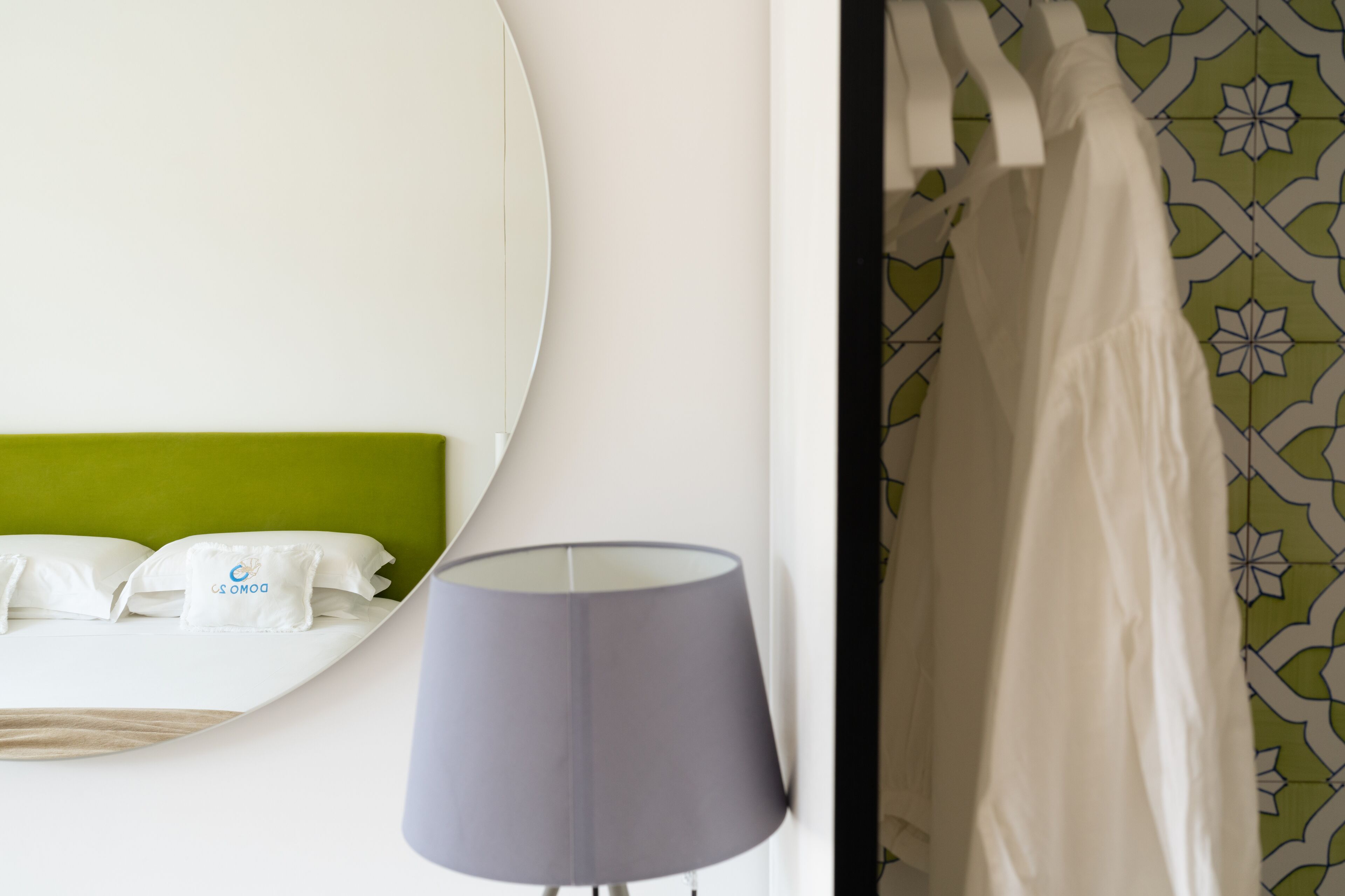 A hotel room with a bed, a round mirror, a lamp, and a patterned curtain.
