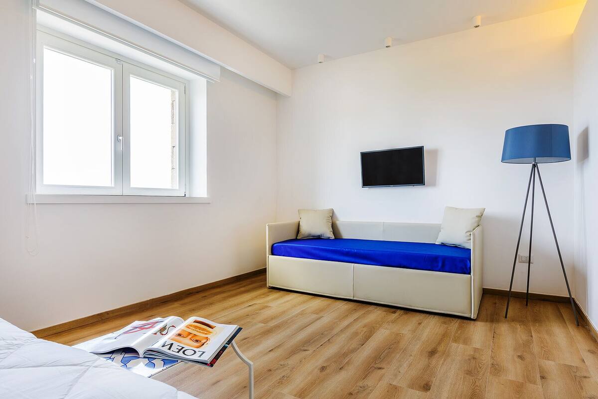 A room with a bed, a TV on the wall, a floor lamp, and a magazine on a table.