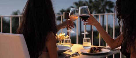 Two people toasting at a table with a view of the sea and mountains in the background.