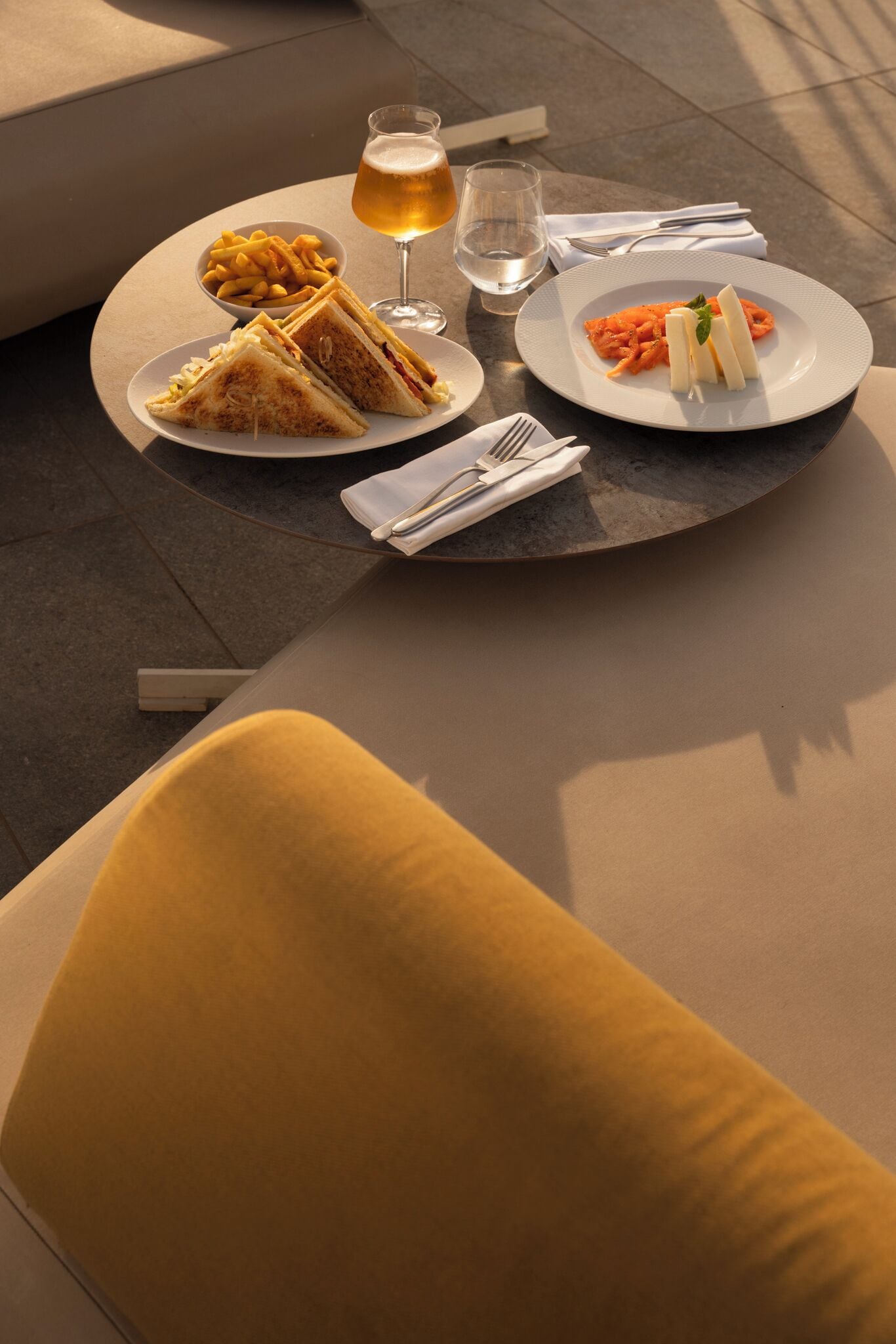 Une table avec un repas composé d’un sandwich, de frites et d’une assiette de pâtes, ainsi qu’un verre de bière et un verre d’eau.