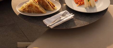 Une table avec un repas composé d’un sandwich, de frites et d’une assiette de pâtes, ainsi qu’un verre de bière et un verre d’eau.