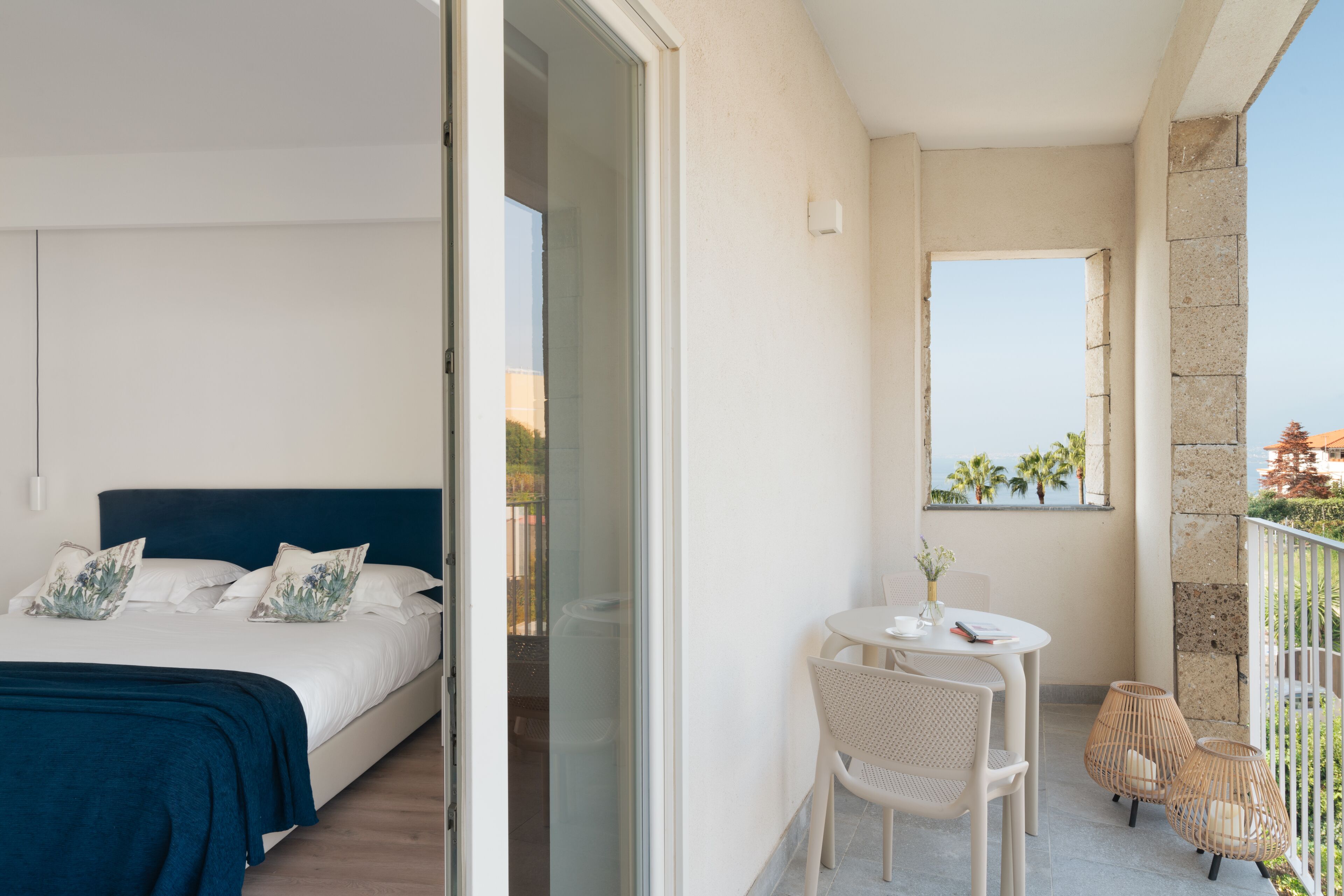 A hotel room with a bed, a balcony with a table and chairs, and a view of the sea.