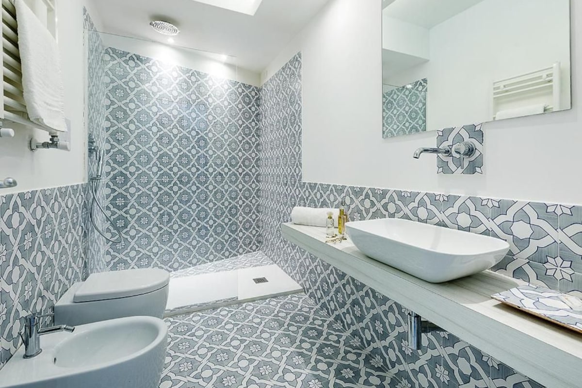 A modern bathroom with patterned tiles, a large sink, a toilet, and a shower area.
