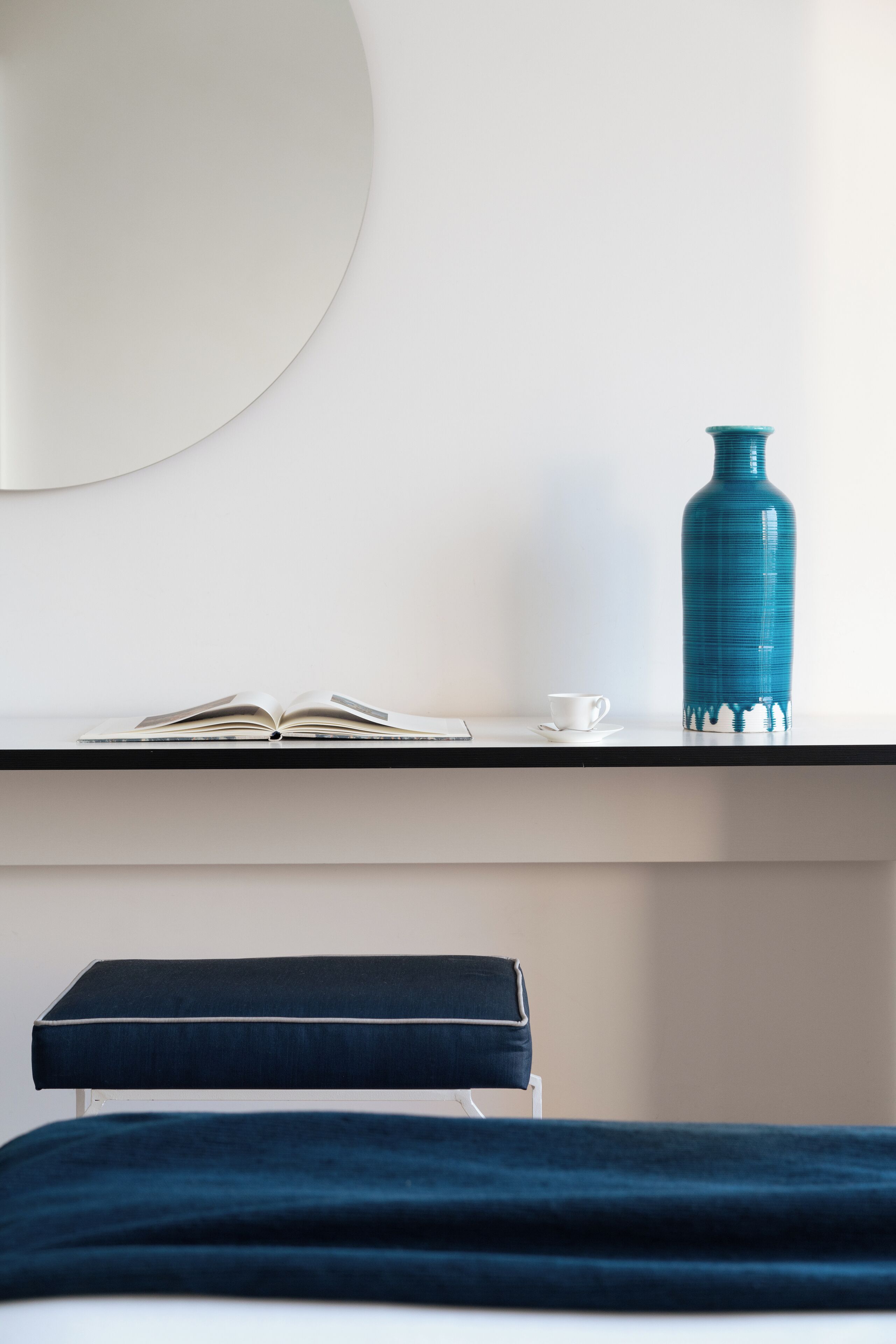 A neatly arranged hotel room with a bed, a bedside table, a blue vase, and an open book.