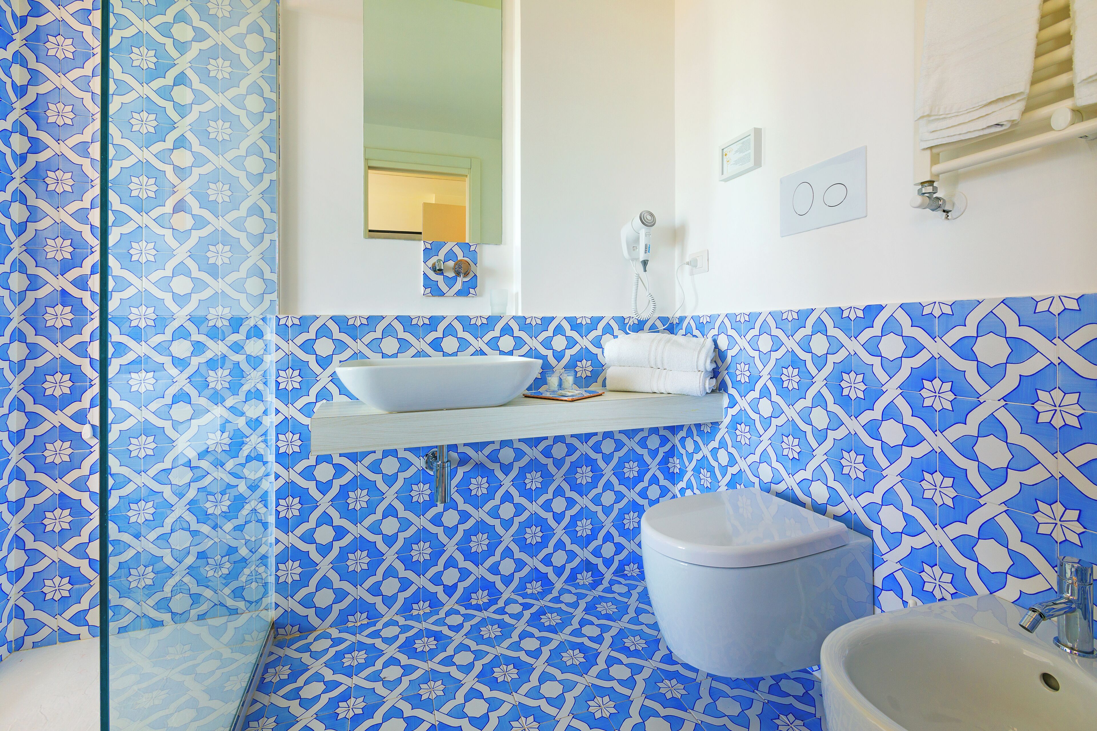 A bathroom with blue patterned tiles, a white sink, a toilet, and a glass shower enclosure.