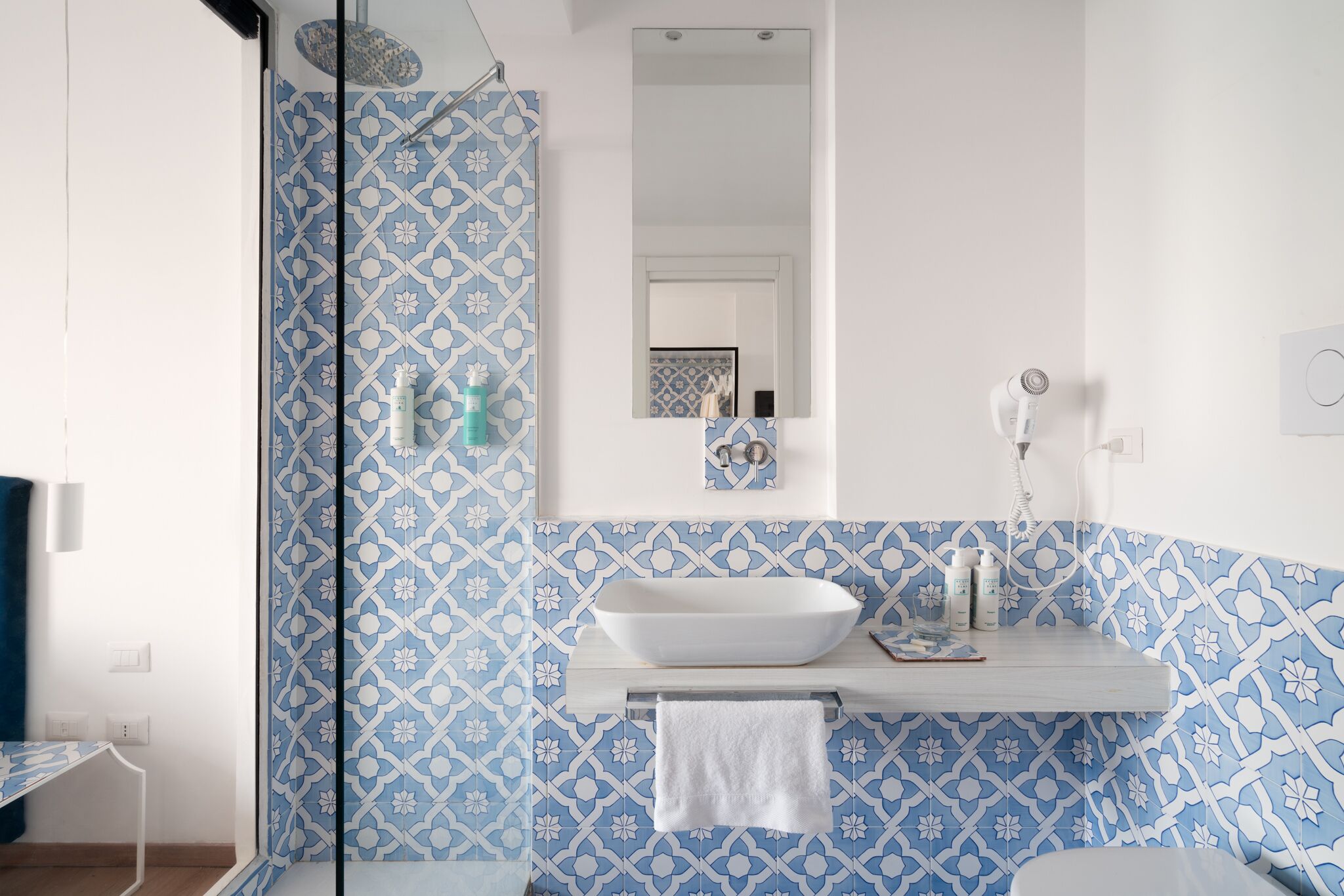 A bathroom with a white sink, blue patterned tiles, a mirror, and a towel hanging on a rack.