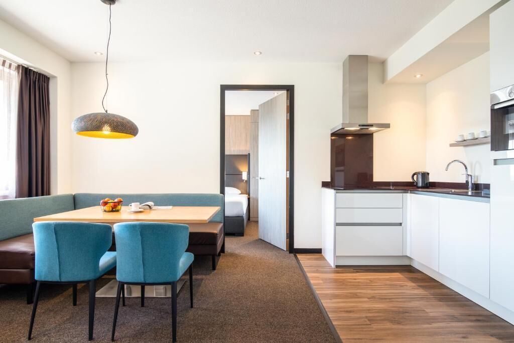Een moderne hotelkamer met een zithoek, kitchenette en uitzicht op de gang.