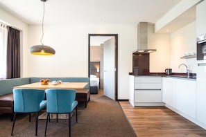 Une chambre d’hôtel moderne dotée d’un coin repas, d’une kitchenette et donnant sur le couloir.