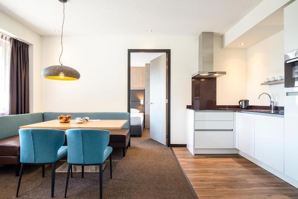 A modern hotel room with a dining area, kitchenette, and a view of the hallway.