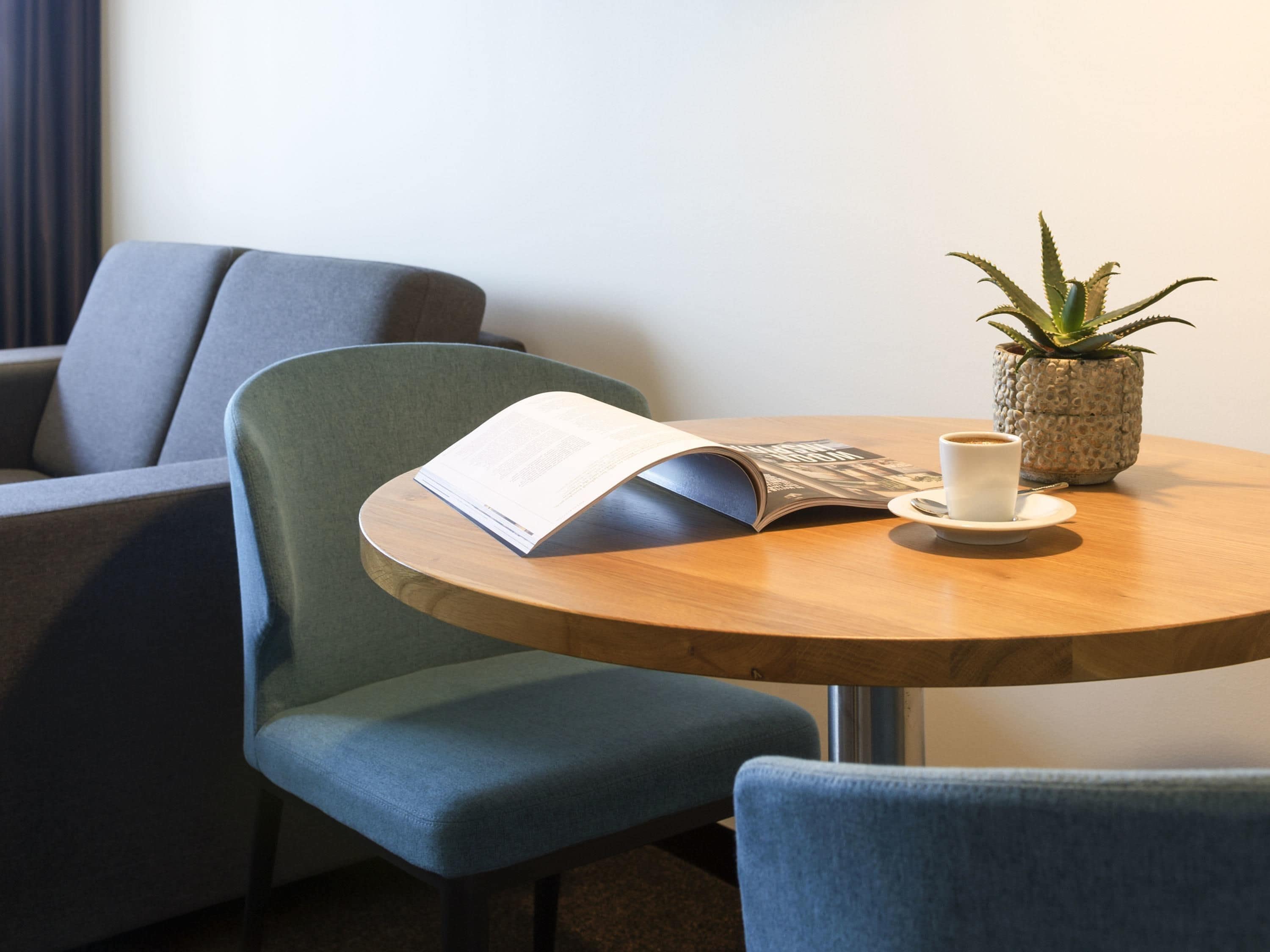 A round wooden table with a book, a cup, and a potted plant.