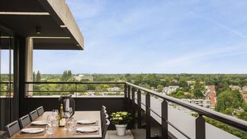 A balcony with a dining table set for four, overlooking a cityscape.