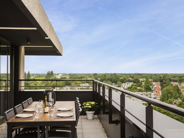 Un balcon avec une table à manger dressée pour quatre personnes, offrant une vue sur le paysage urbain.