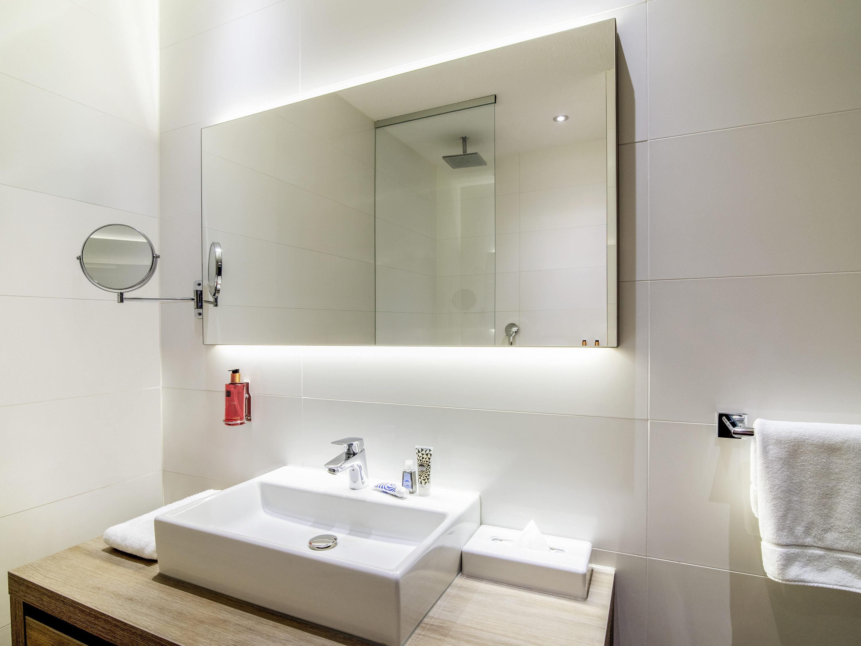 Une salle de bain moderne avec un grand miroir, un lavabo et un porte-serviettes.