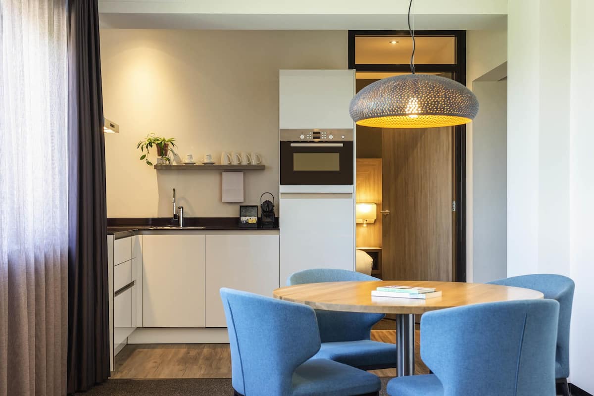 Une chambre d’hôtel moderne dotée d’un coin repas, d’une cuisine et d’un espace nuit séparé.