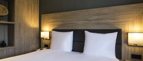A hotel room with a large bed, two bedside lamps, a wooden headboard, and a small nightstand with a red book.