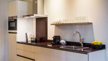 A modern kitchen with a built-in oven, a coffee machine, a sink, and a shelf with glasses.