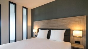Una habitación de hotel con una cama grande, dos lámparas de noche y una mesita de noche.