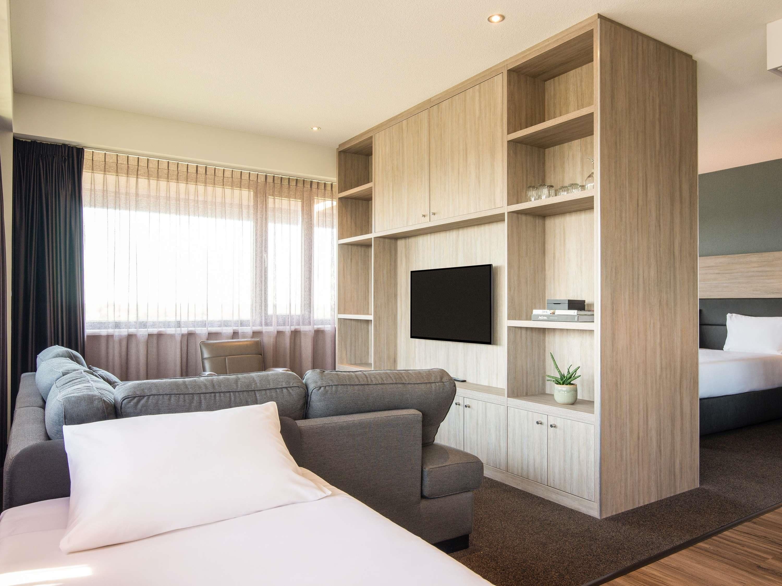Een moderne hotelkamer met een grote bank, een bed, een aan de muur bevestigde televisie en inbouwplanken.