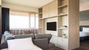 Een moderne hotelkamer met een grote bank, een bed, een aan de muur bevestigde televisie en inbouwplanken.