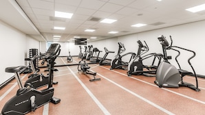 Une salle de sport équipée de nombreux appareils d’exercice, notamment des tapis de course et des vélos elliptiques, disposés en rangées.