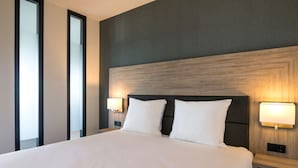 Een moderne hotelkamer met een groot bed, twee nachtkastjes met lampen, en een donker hoofdeinde.