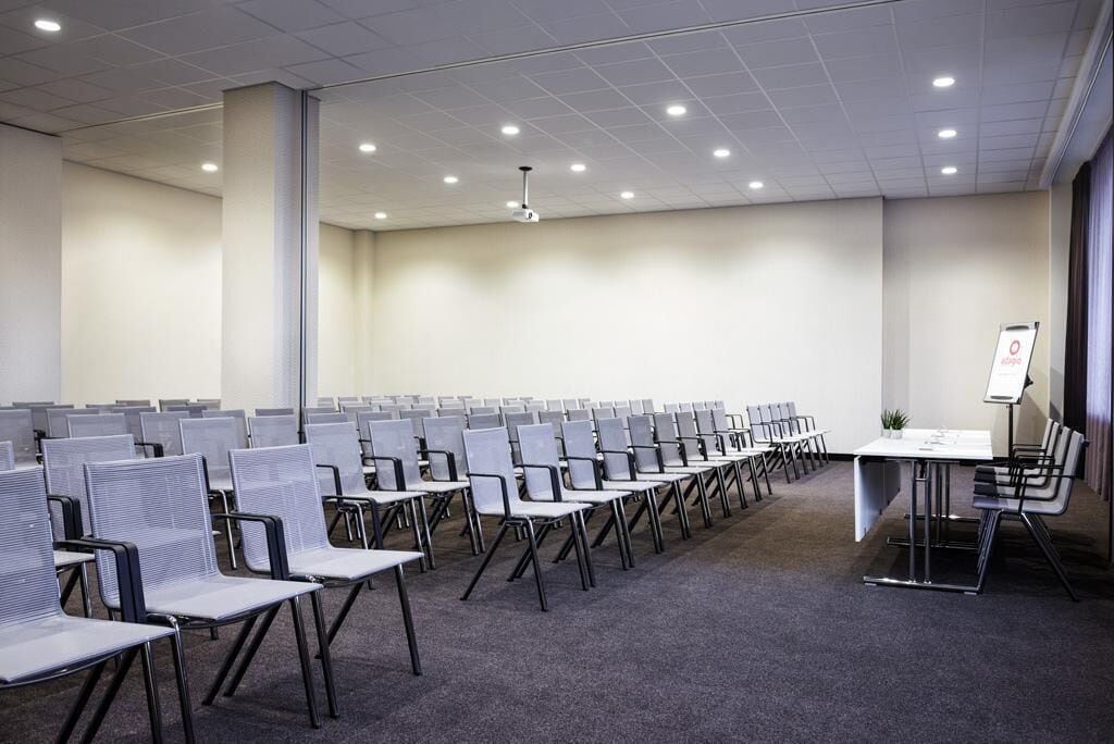 A conference room with rows of chairs, a projector screen, and a table with a laptop.