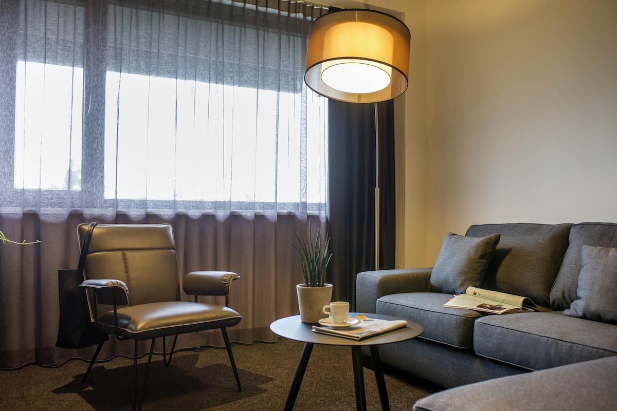 A modern hotel room with a sofa, armchair, and a floor lamp.
