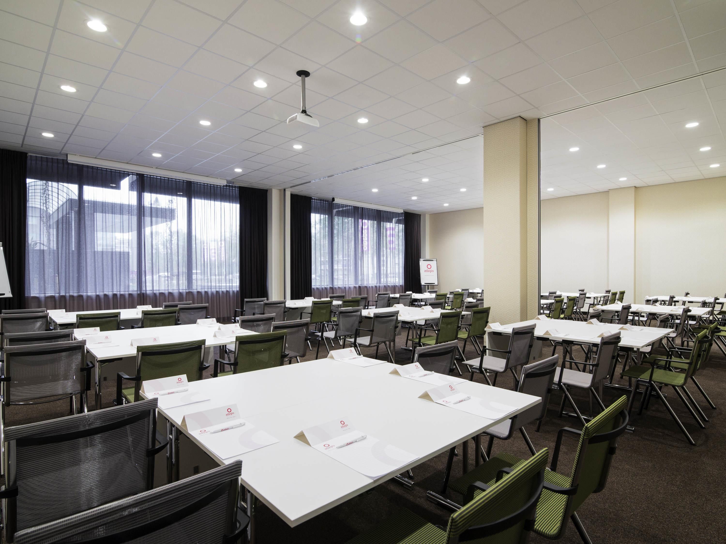 A conference room with multiple tables and chairs, large windows with curtains, and a whiteboard.